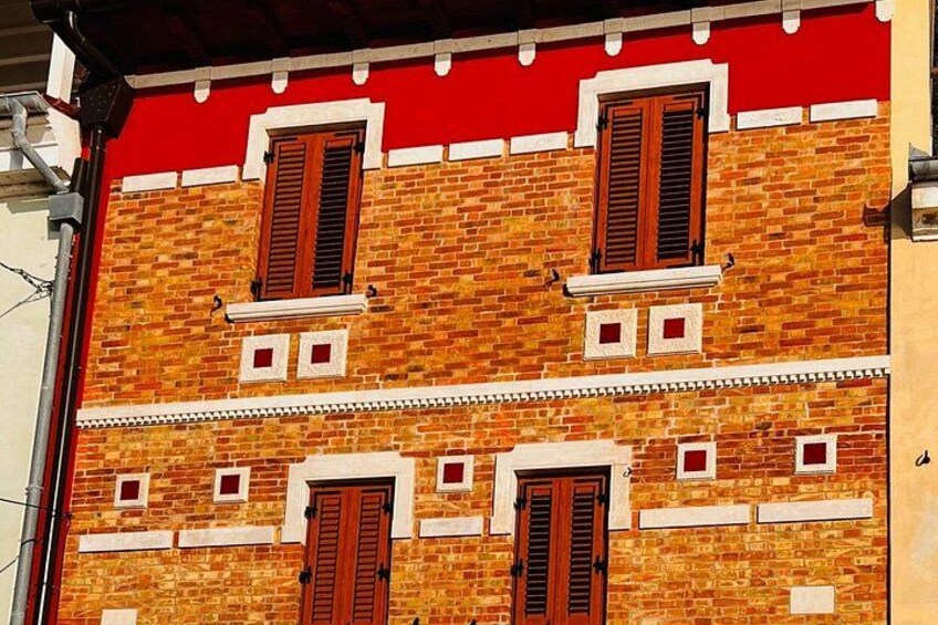 A brick building with red and white trim, multiple windows with shutters, and a red awning. 3