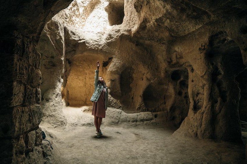 A person standing in a cave with a rock formation overhead. 5