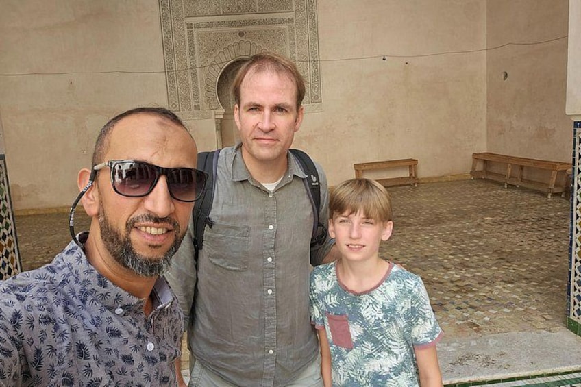 Drie personen staan in een binnenplaats met versierde vloertegels en bankjes. 3