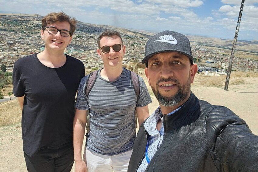 Three people standing on a hill with a cityscape in the background. 3