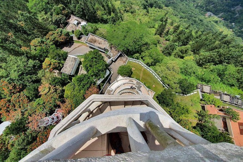 Un escalier en pierre qui monte une colline, offrant une vue sur une zone boisée et un bâtiment situé au loin. 3