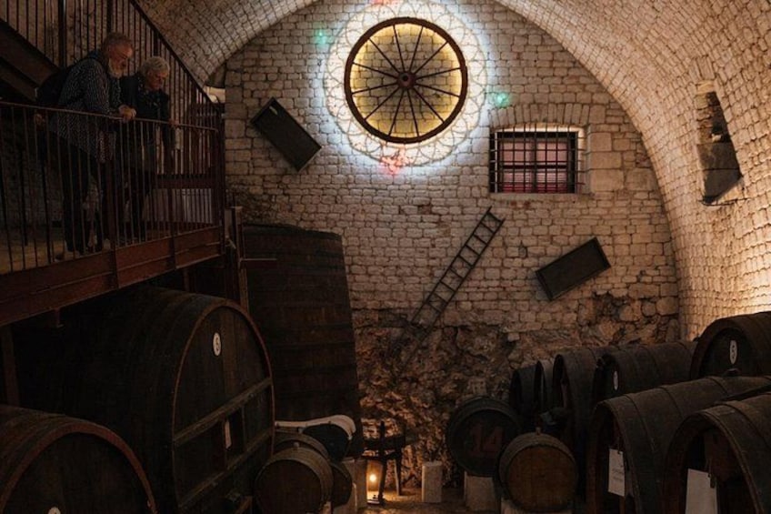An underground wine cellar with stone walls, wooden barrels, and a circular skylight. 5