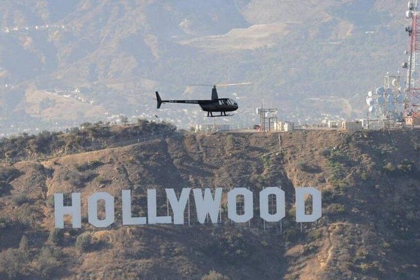 A helicopter flying over a hilly area with the word 'HOLLYWOOD' prominently displayed. 1