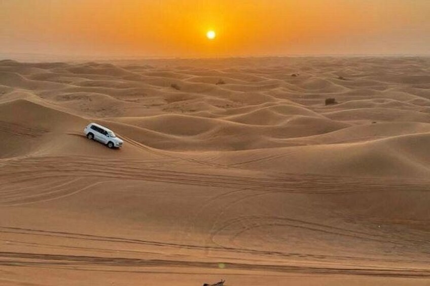 Un véhicule blanc se déplaçant sur des dunes de sable au coucher du soleil. 2