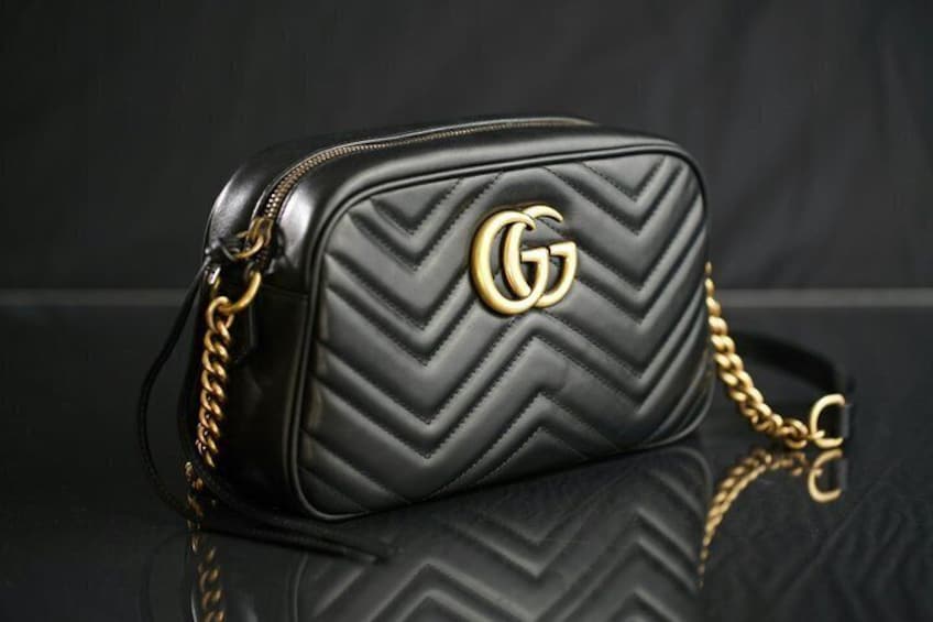 A black handbag with a gold logo and a gold chain strap. 1