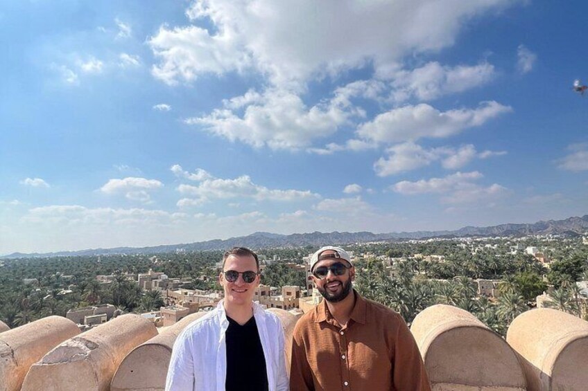 Dos personas de pie en una terraza con un paisaje urbano y montañas al fondo. 4