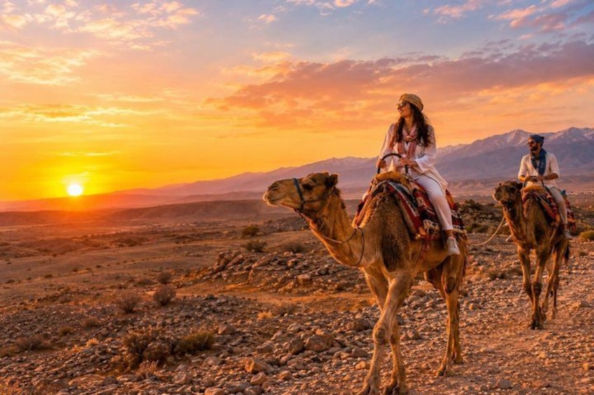 Two people riding camels in a desert landscape during sunset. 2