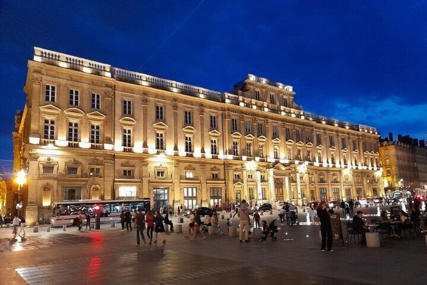 Un edificio histórico con ventanas iluminadas y una plaza animada en su fachada. 4