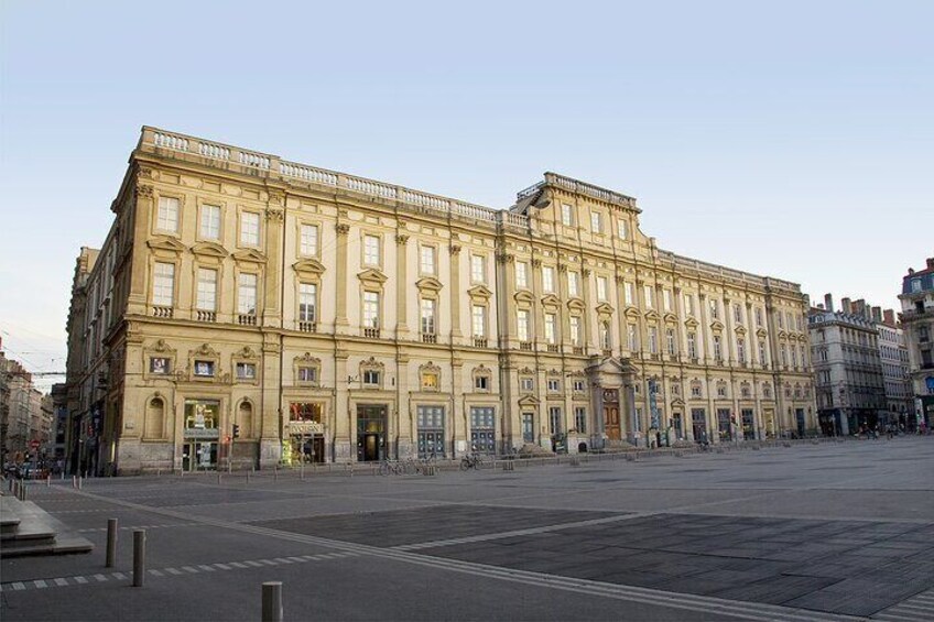 Un edificio grande e histórico con arquitectura clásica, una amplia plaza frente a él y un cielo despejado. 5