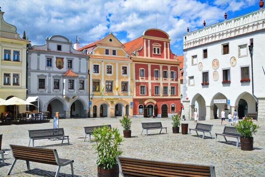 Una piazza lastricata con panchine e piante in vaso, circondata da edifici storici colorati. 1