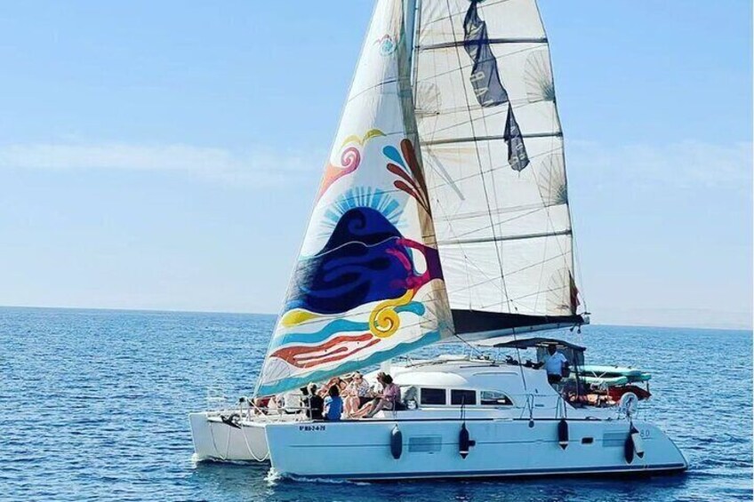 A sailboat with a colorful sail design, people on board, and calm sea. 1