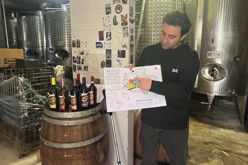 A person holding a map and a wine bottle in a cellar with barrels and stainless steel tanks. 3