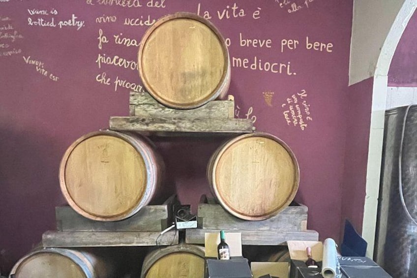 Wooden barrels stacked in a pyramid formation against a wall with handwritten text. 5