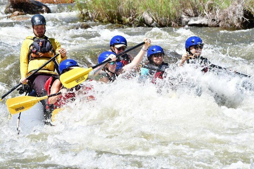 A group of people in a yellow kayak navigating a river with white water rapids. 3