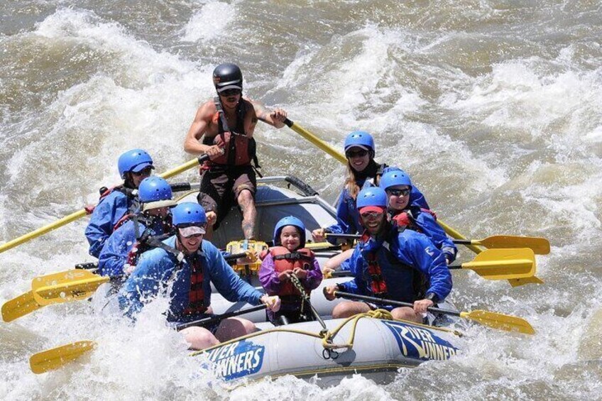 A group of people in a raft with paddles, navigating through rough water. 2
