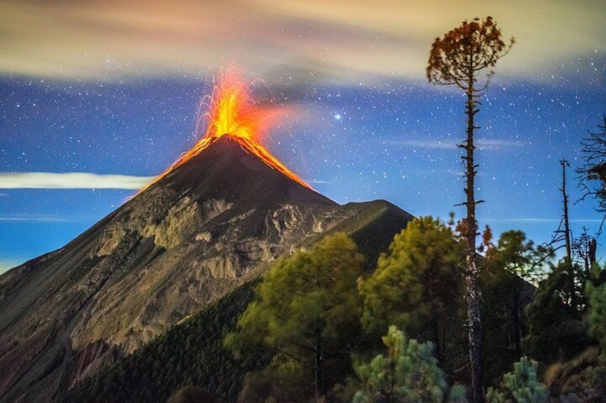 Un volcan en éruption, avec de la lave qui coule le long de ses flancs, entouré d’arbres et surplombant un ciel étoilé. 3