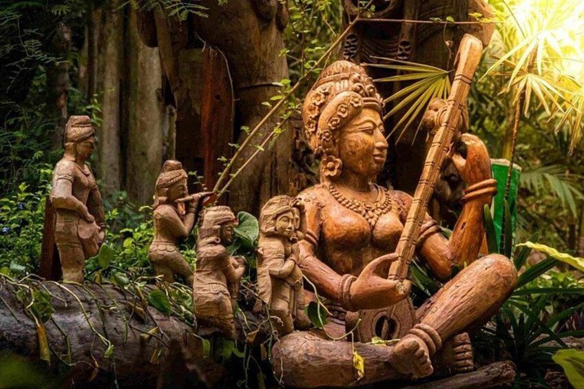 A wooden sculpture of a deity with multiple figures, set in a forested area with trees and foliage. 4
