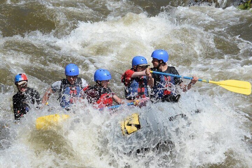 A group of people in a white raft with blue helmets navigating through a river with white water rapids. 4