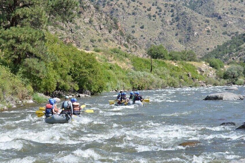 People rafting down a river surrounded by greenery and hills. 1