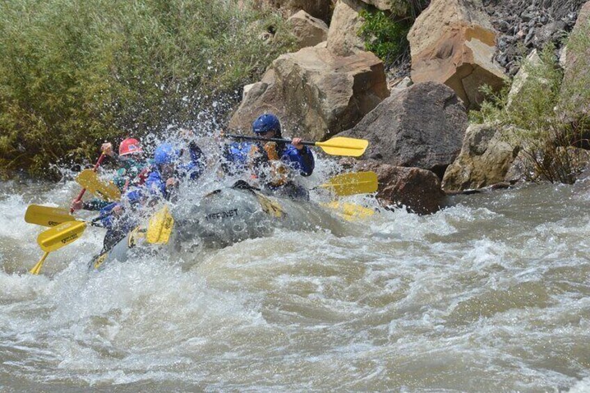 A group of kayakers navigating through a river with rapids, surrounded by large rocks and greenery. 2