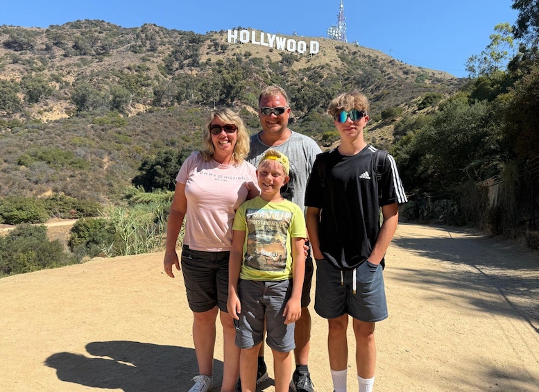 A family standing in front of the Hollywood sign with a hilly landscape in the background. 1