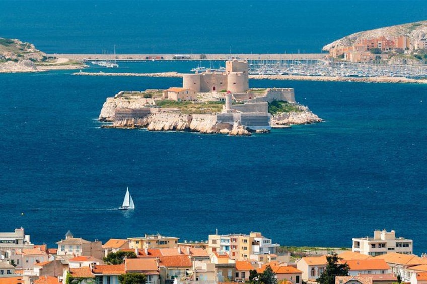 Una cittadina costiera con una struttura imponente simile a una fortezza, circondata da acqua, una barca a vela e edifici residenziali. 1