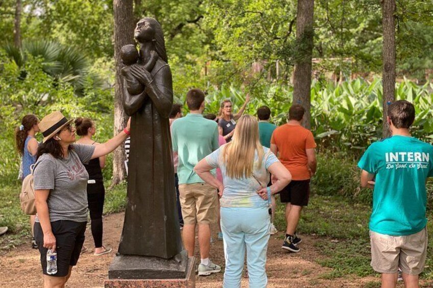 A group of people standing around a statue in a park. 2
