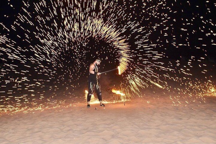A person performing fire juggling in a sandy area with sparks flying. 3