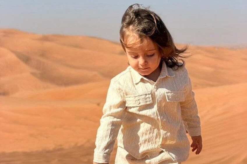 Et barn i en hvid skjorte går i en ørken med sanddyner i baggrunden. 3