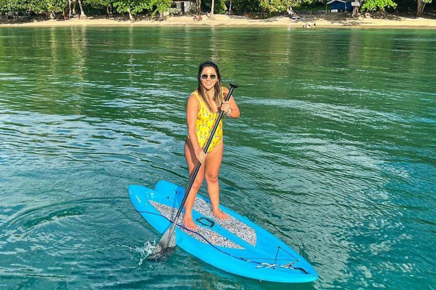 A person paddleboarding on a calm body of water with a beach in the background. 4