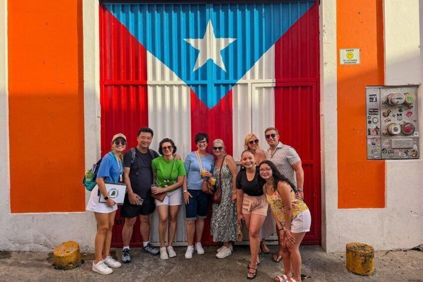 A group of people posing in front of a building with a large flag featuring a star and stripes. 4