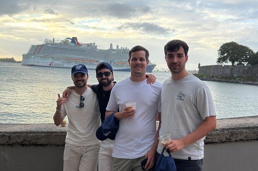 Three people standing by a waterfront with a cruise ship in the background. 3