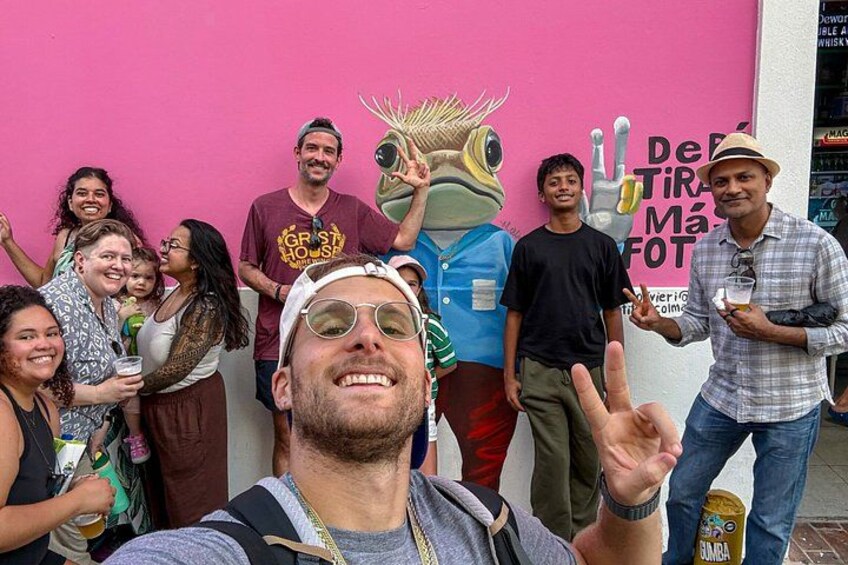 A group of people posing in front of a pink wall with a cartoon character and text. 2