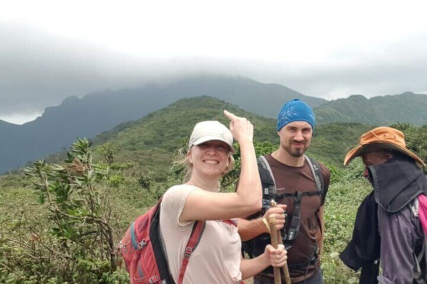 Drie mensen wandelen op een berg, met weelderige begroeiing en mistige bergen op de achtergrond. 4
