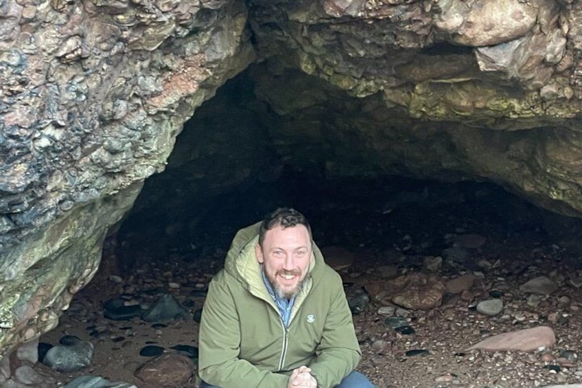 A person sitting in a cave with rocky walls and a ground covered in small stones. 5