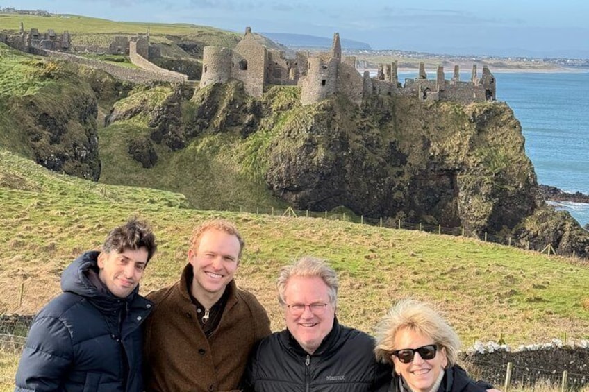 A group of people in front of a historic castle on a cliff overlooking the sea. 1