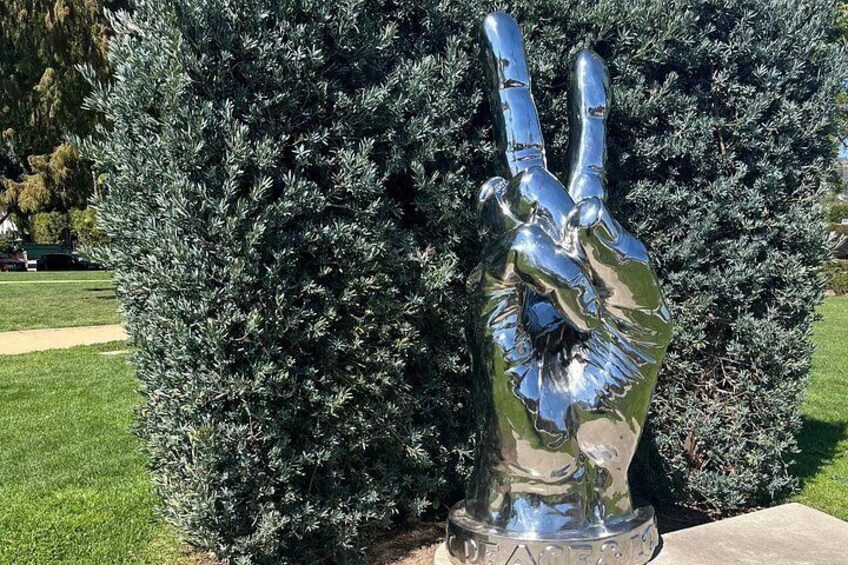 A metallic hand sculpture with a peace sign in front of a dense bush. 3