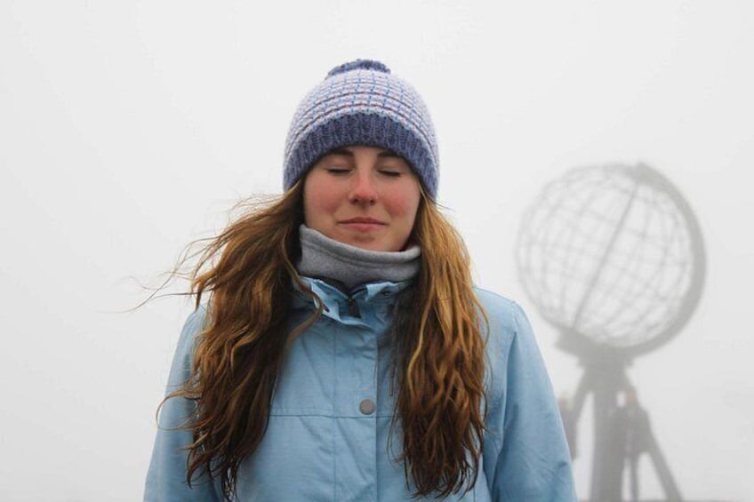 Une personne portant une veste bleue et un bonnet en tricot, debout devant un arrière-plan brumeux, avec l’ombre d’un globe. 2
