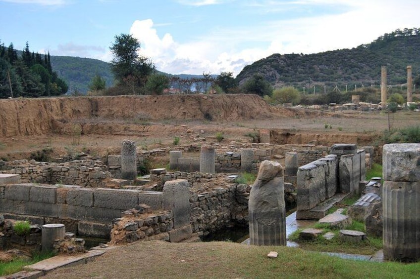 Ancient ruins with stone columns and walls, set against a backdrop of hills and trees. 4