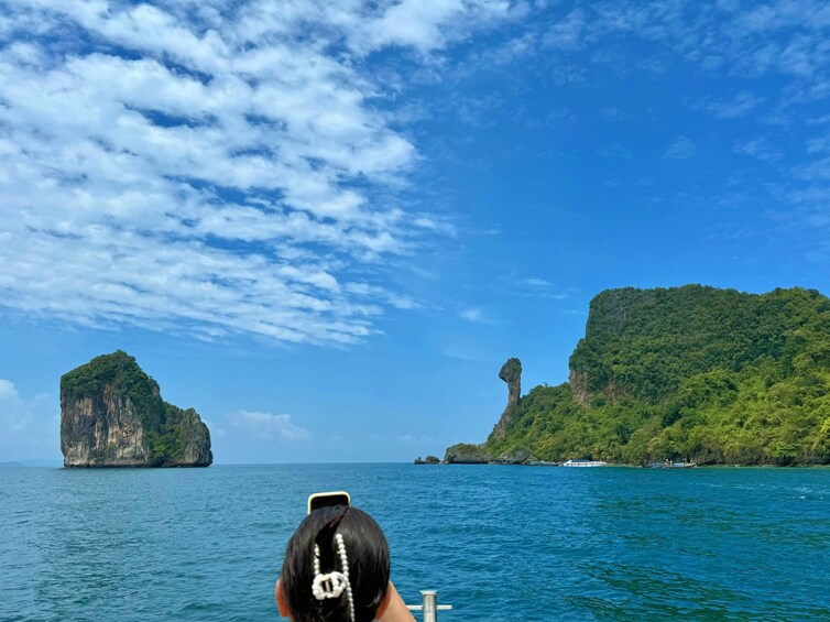 A boat with a person in the foreground, a large rock formation, and a smaller island with dense green foliage in the background. 5