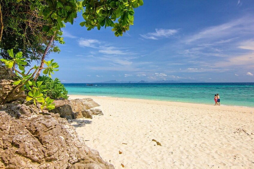A sandy beach with clear turquoise water, rocky outcrops, and a distant mountain range. 1