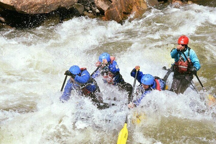 A group of people in blue helmets and life jackets navigating a white water rapids in a kayak. 4