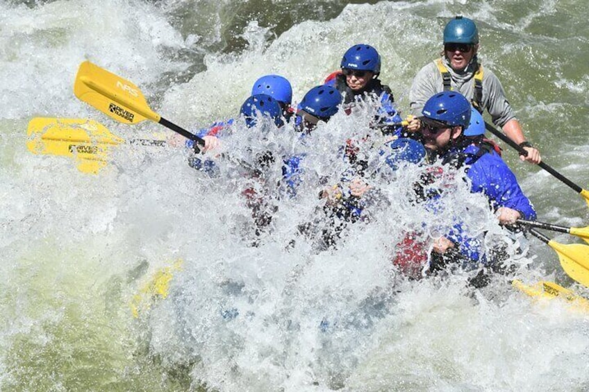 A group of people in a blue kayak navigating through white water rapids. 1