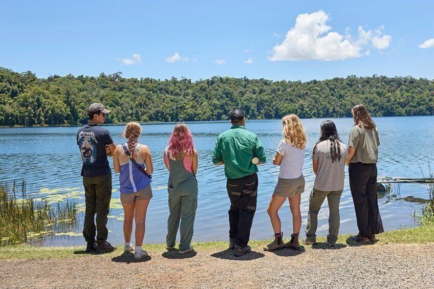 A group of people standing by a lake with a forested shoreline. 3