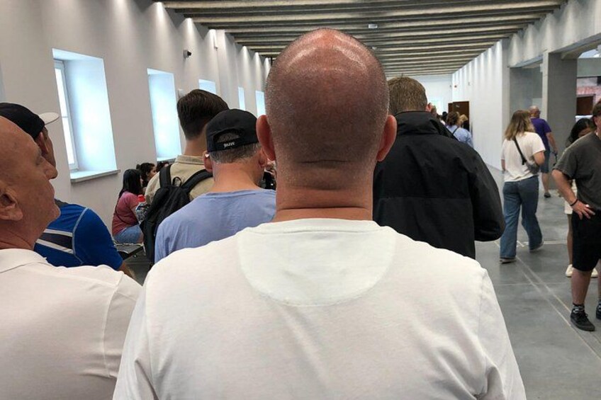 Un grupo de personas caminando por un pasillo con paredes blancas y ventanas rectangulares. 5