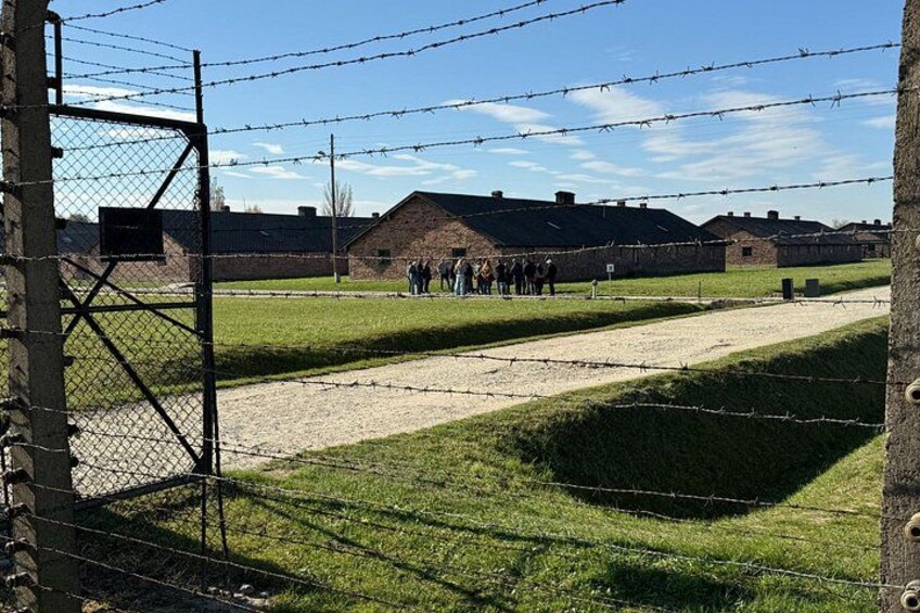 Una cerca de alambre de púas, un campo cubierto de hierba y edificios de ladrillo al fondo. 4