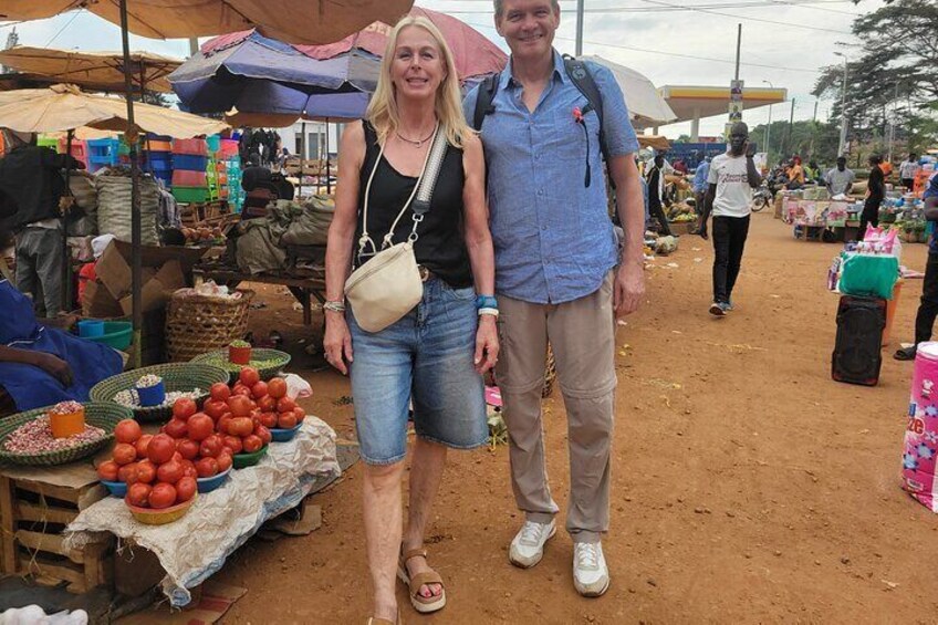 Two people standing at a market with various fruits and vegetables on display. 2