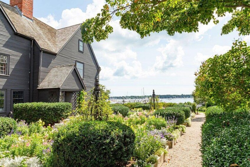 A house with a gravel path leading to a body of water, surrounded by lush greenery and flowering plants. 5