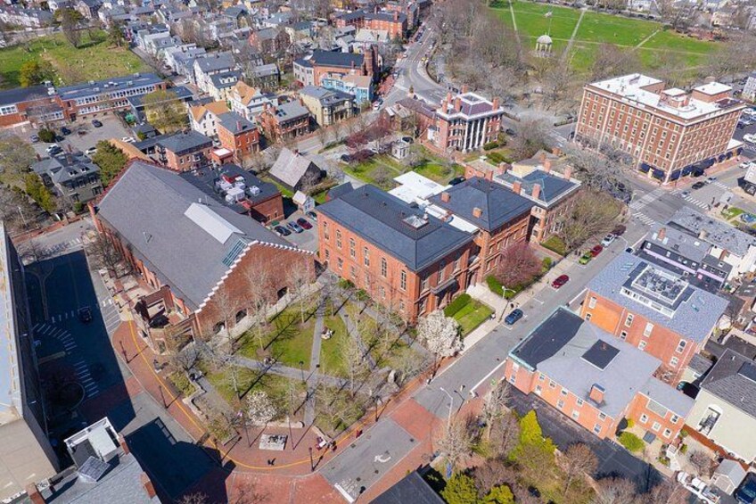 An aerial view of a town with historic buildings, a large brick structure, and a green field. 4