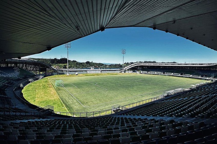 An empty stadium with a football field, seating, and floodlights. 3